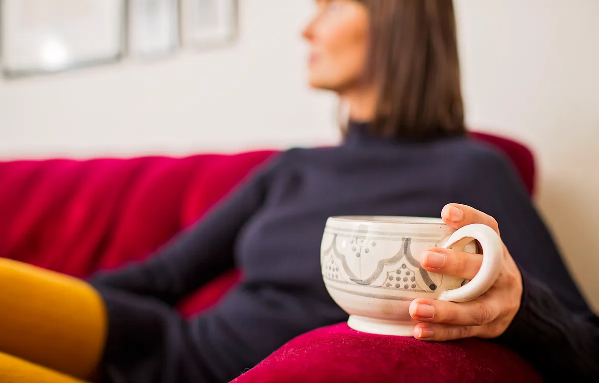 Žena drži šalicu čaja i sjedi na kauču; koncept živjeti s gastritisom