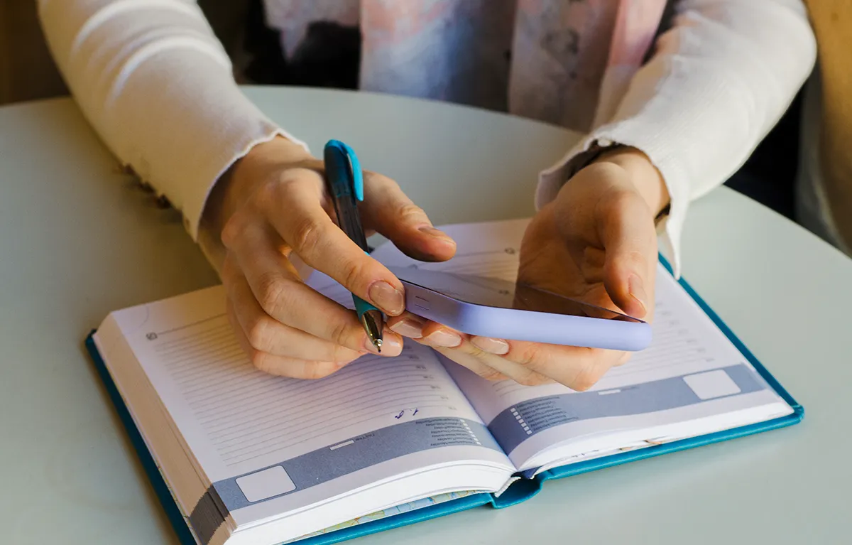 Neprepoznatljiva žena drži mobitel i kemijsku nad dnevnikom; koncept živjeti s gastritisom