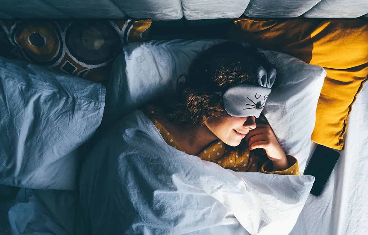 Žena spava u krevetu s maskom za oči; koncept živjeti s gastritisom