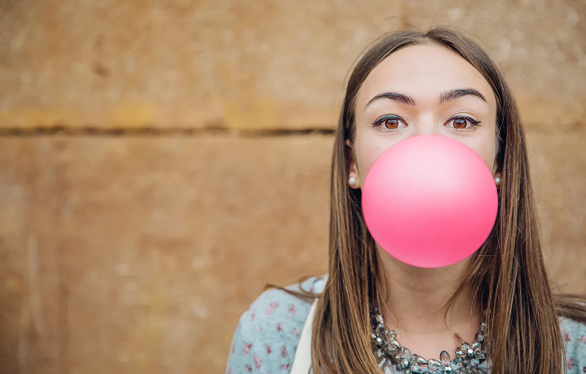 Mlada žena napuhuje veliki rozi balon žvakaće gume; koncept kava i kofein