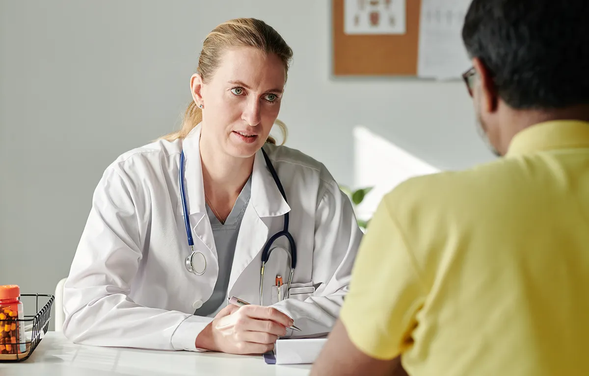 Ozbiljna liječnica u ordinaciji razgovara s pacijentom prikazanim s leđa; koncept rak mokraćnog mjehura, zanemarena a učestala bolest.