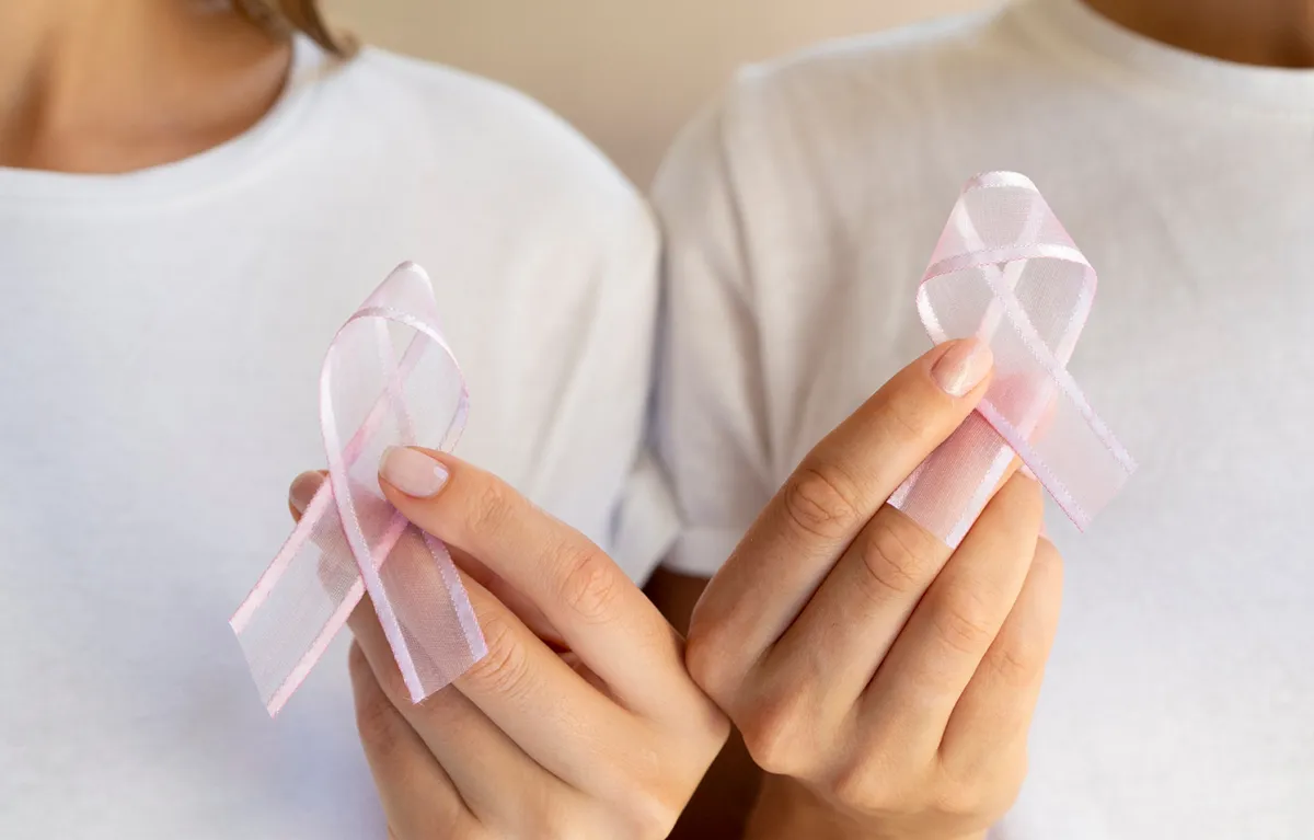 Dvije ženske ruke drže znak podrške za oboljele od raka dojke; koncept rekonstrukcija dojke nakon raka dojke