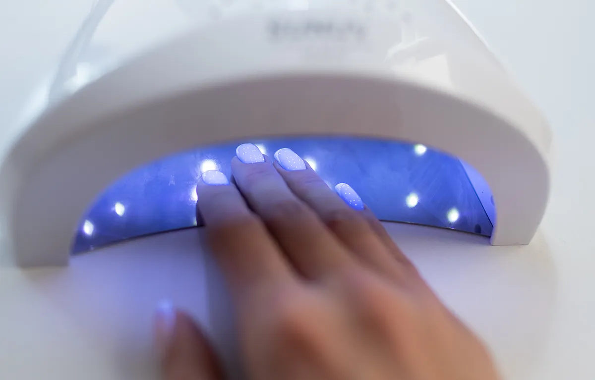 Ruka s gel lakom na noktima u UV/LED lampi; koncept toksičnost TPO-a