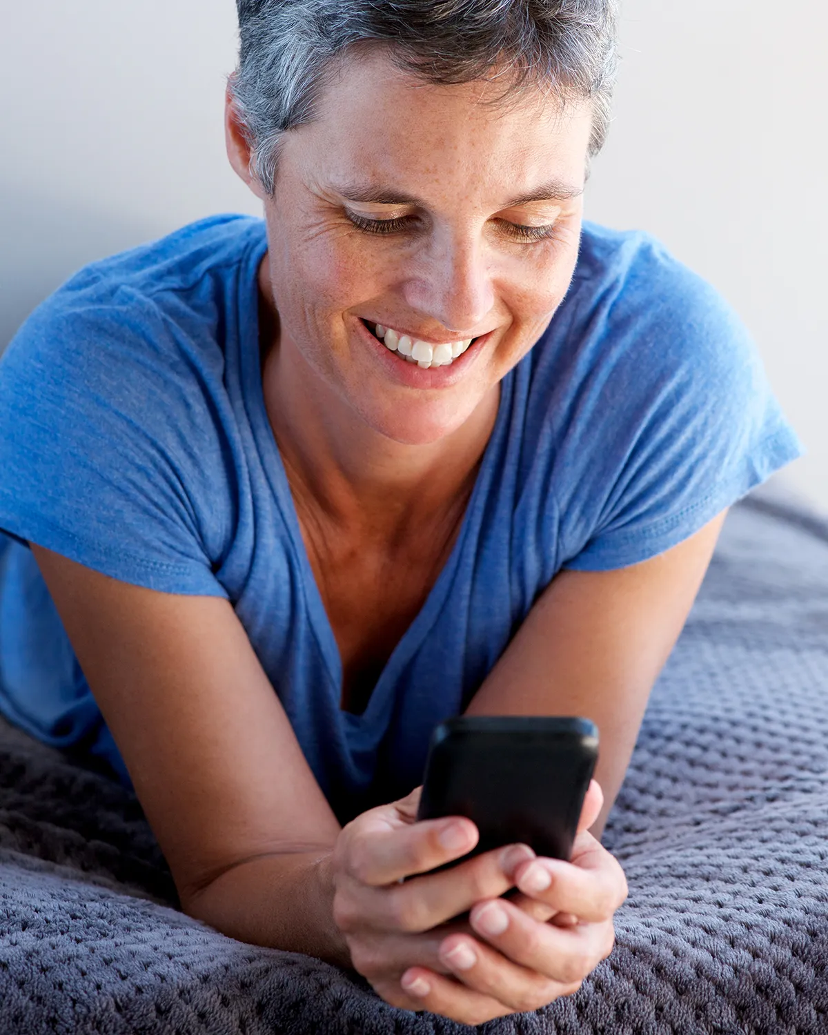 Žena srednje životne dobi s osmijehom gleda u mobitel; kontakt za čitatelje