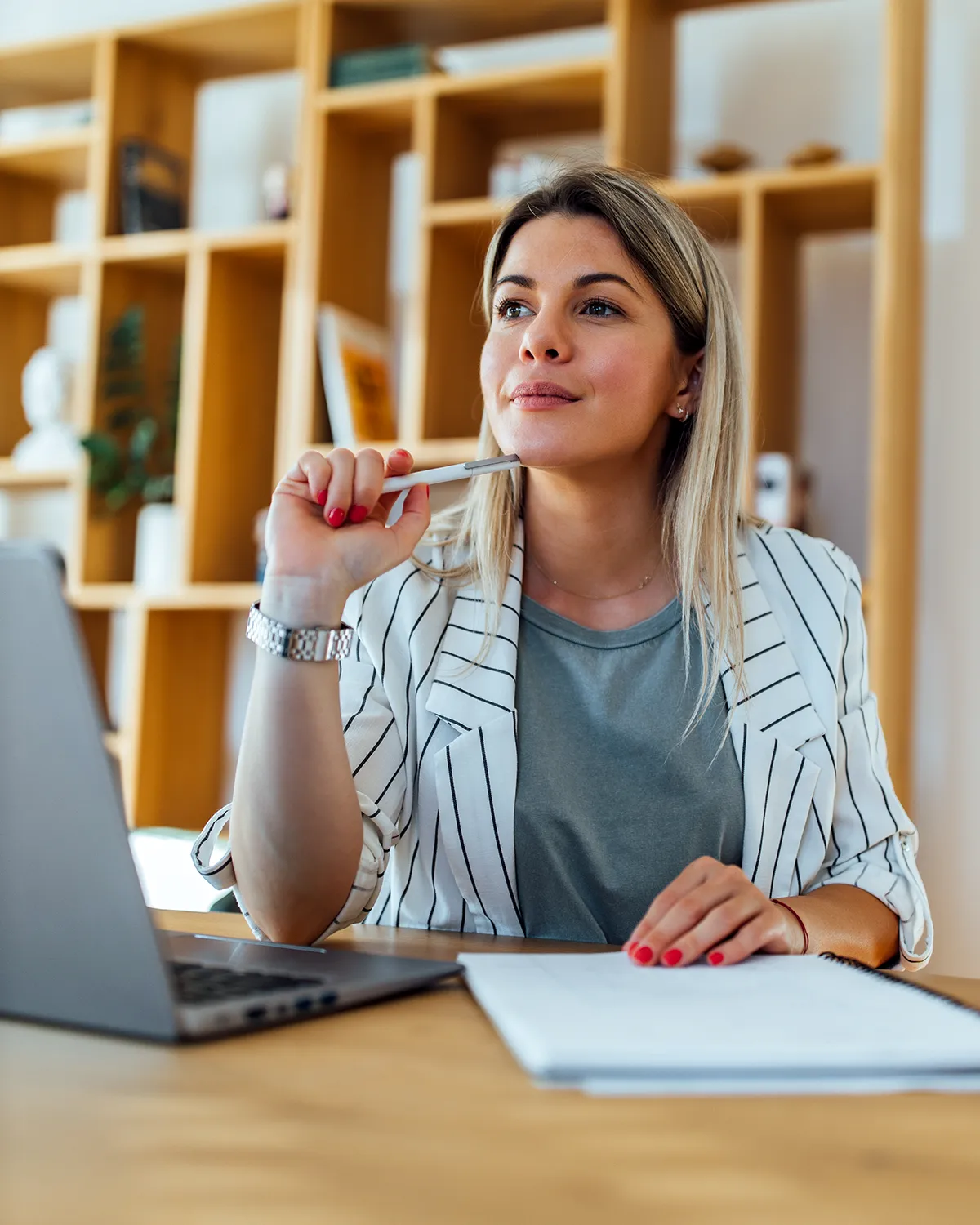 Zamišljena i zadovoljna žena uz laptop i bilježnicu; kontakt za suradnike