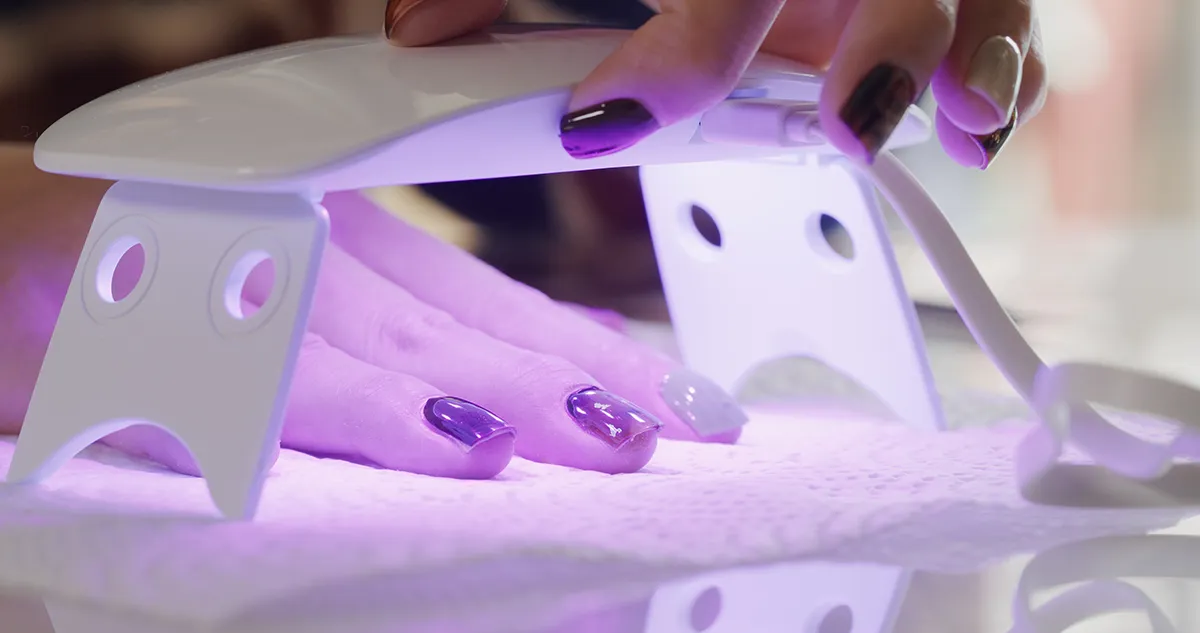 Krupni plan ruke s gel lakom na noktima ispod kućne UV/LED lampe; koncept TPO i HEMA
