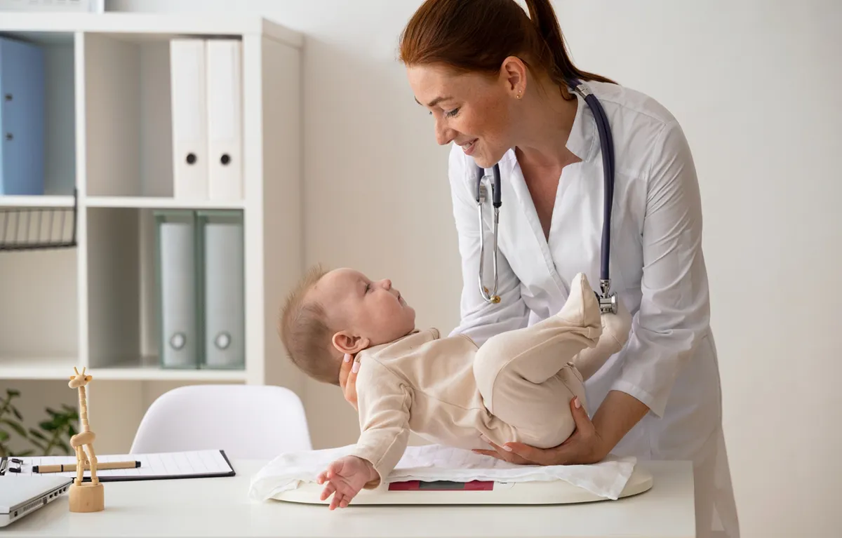 Pedijatrica u ordinaciji drži malenu bebu iznad stola; koncept pedijatar i broj pacijenata u RH