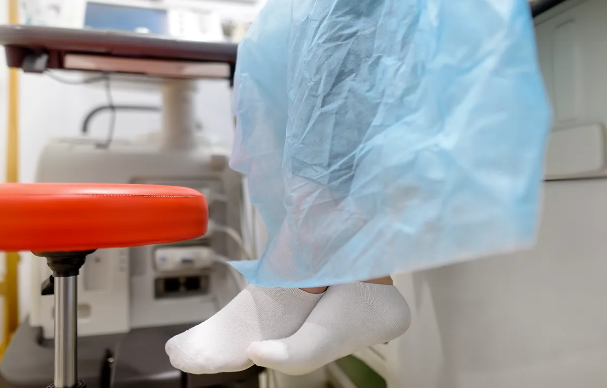 Noge pacijentice obučene u medicinsku haljinu, sjedi na bolesničkom pregledu; koncept privatnost tijekom pregleda