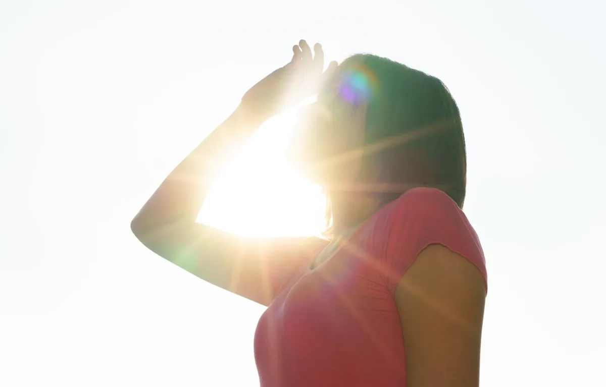 Žena se rukom štiti od jakog sunca; koncept vrućine i krvni tlak