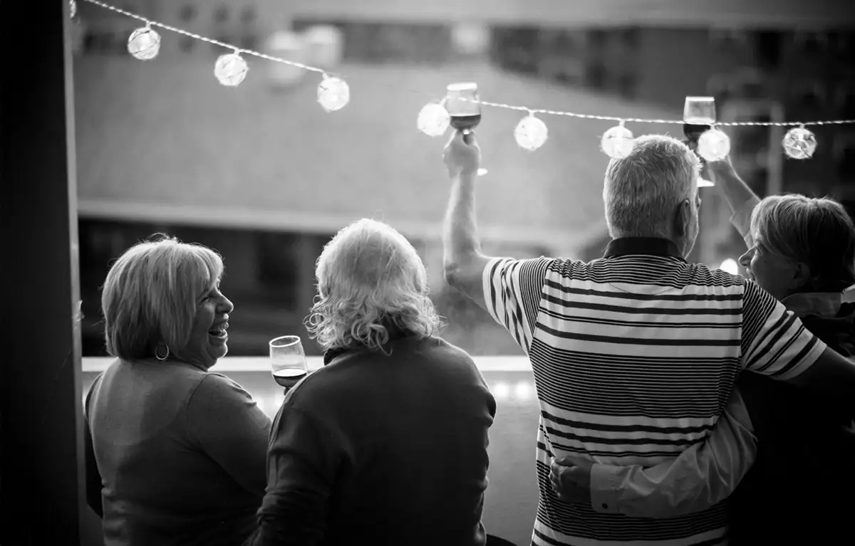 Dvije starije žene i jedan muškarac okrenuti leđima na crno bijeloj fotografiji, a iznad njih su lampice upaljene; koncept briga za starije