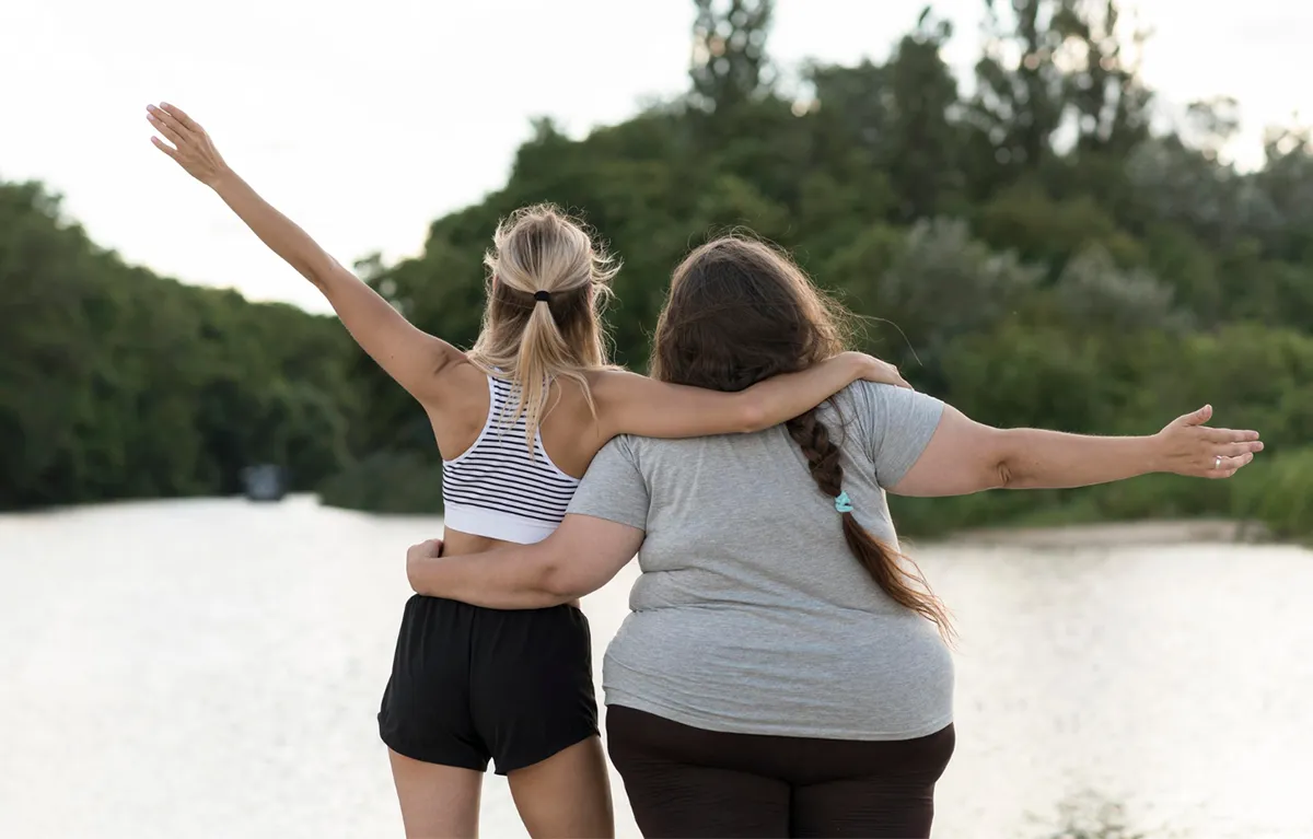 lijek-debljina-esencijalni-lijekovi Dvije žene zagrljene i slikane s leđa, jedna vitka, a druga pretila; koncept lijekovi za debljinu i dijabetes