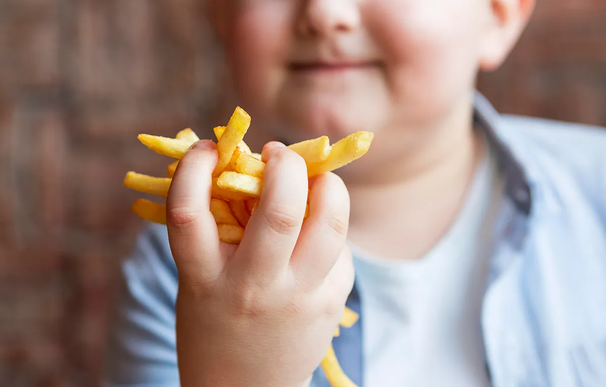 Pretili dječak u šaci čvrsto drži pržene krumpiriće; koncept pretilost djece