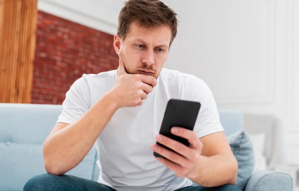 prevare-HZZO Mladić sjedi na dvosjedu i zabrinuto gleda u mobitel u ruci; koncept HZZO lažne poruke