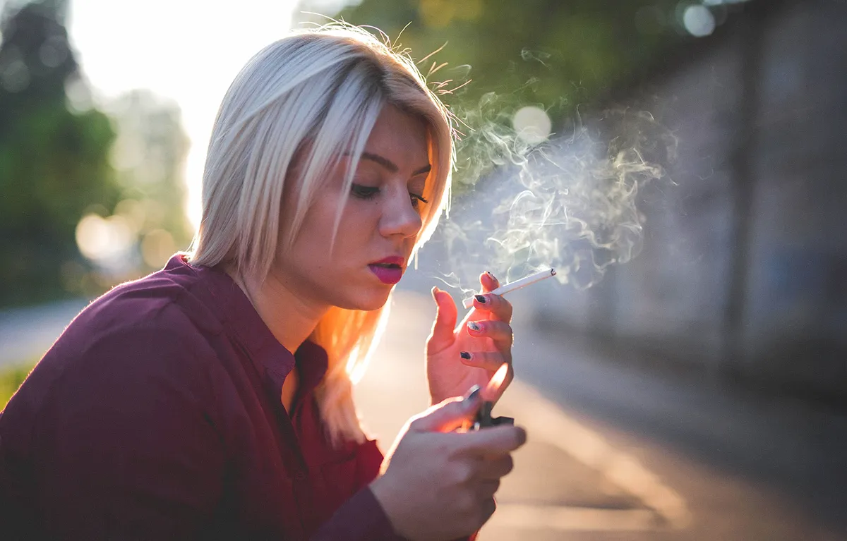 sto-sve-cigareta-cini-organizmu Mlada žena u protusvjetlu sjedi i drži upaljenu cigaretu i upaljač; koncept što sve cigareta čini organizmu