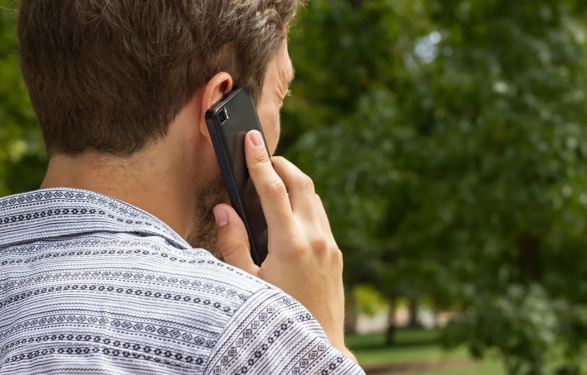 Muškarac prikazan odostraga razgovara na mobitel; koncept lažni pozivi doktora koji traže novac