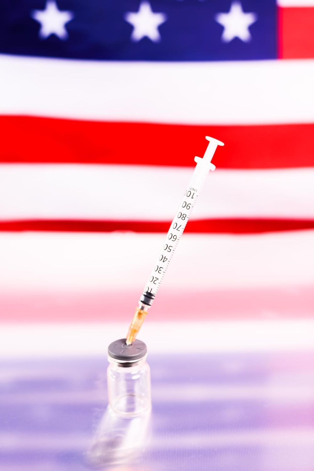 Cijepljenje u Americi Šprica zabijena u staklenu bočici, a u pozadini američka zastava.