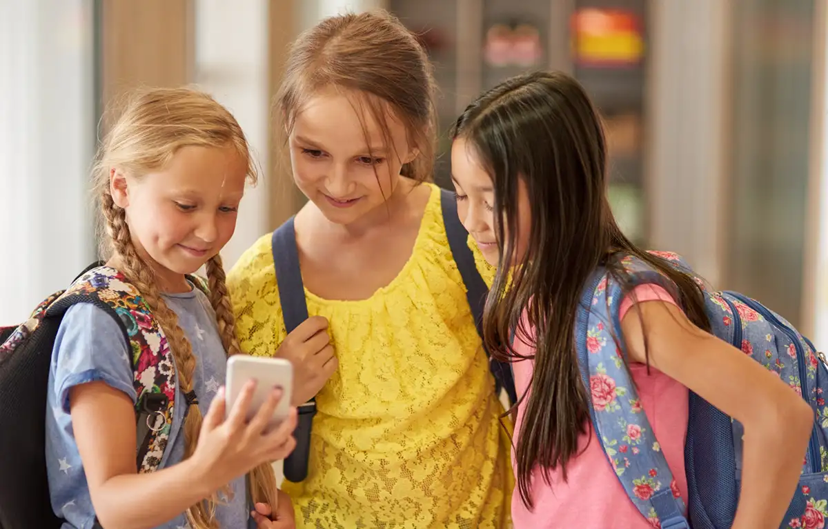 djeca-mreze-skola-Prizma Tri školske djevojčice gledaju u mobitel; koncept zabraniti društvene mreže mlađima od 16 godina