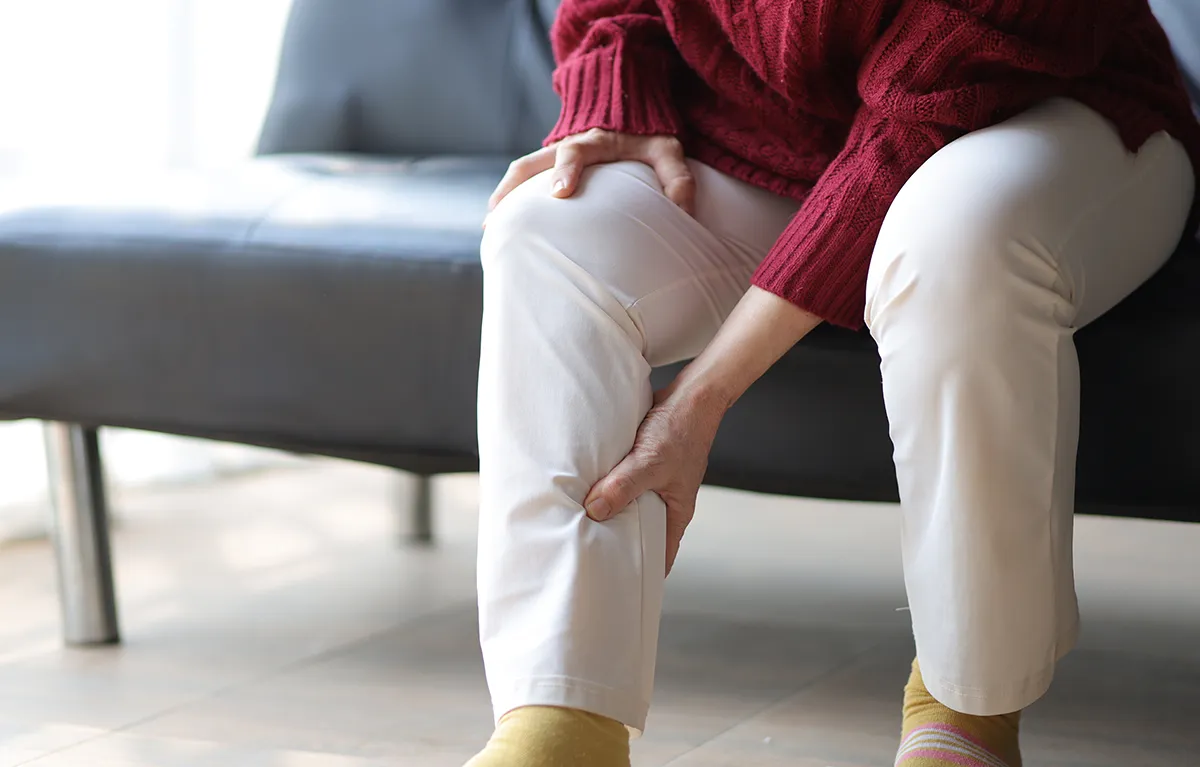 Neprepoznatljiva žena srednje životne dobi drži se rukom za bolnu i oteknutu potkoljenicu; limfedem i druge nuspojave, zračenje ranog raka dojke 