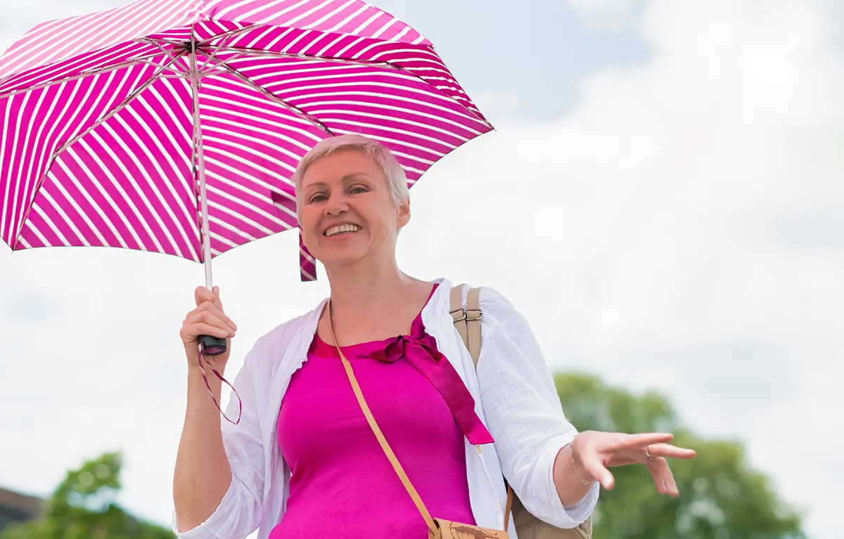 Žena srednje dobi u roza majici nosi roza kišobran za zaštitu od sunca; zračenje ranog raka dojke