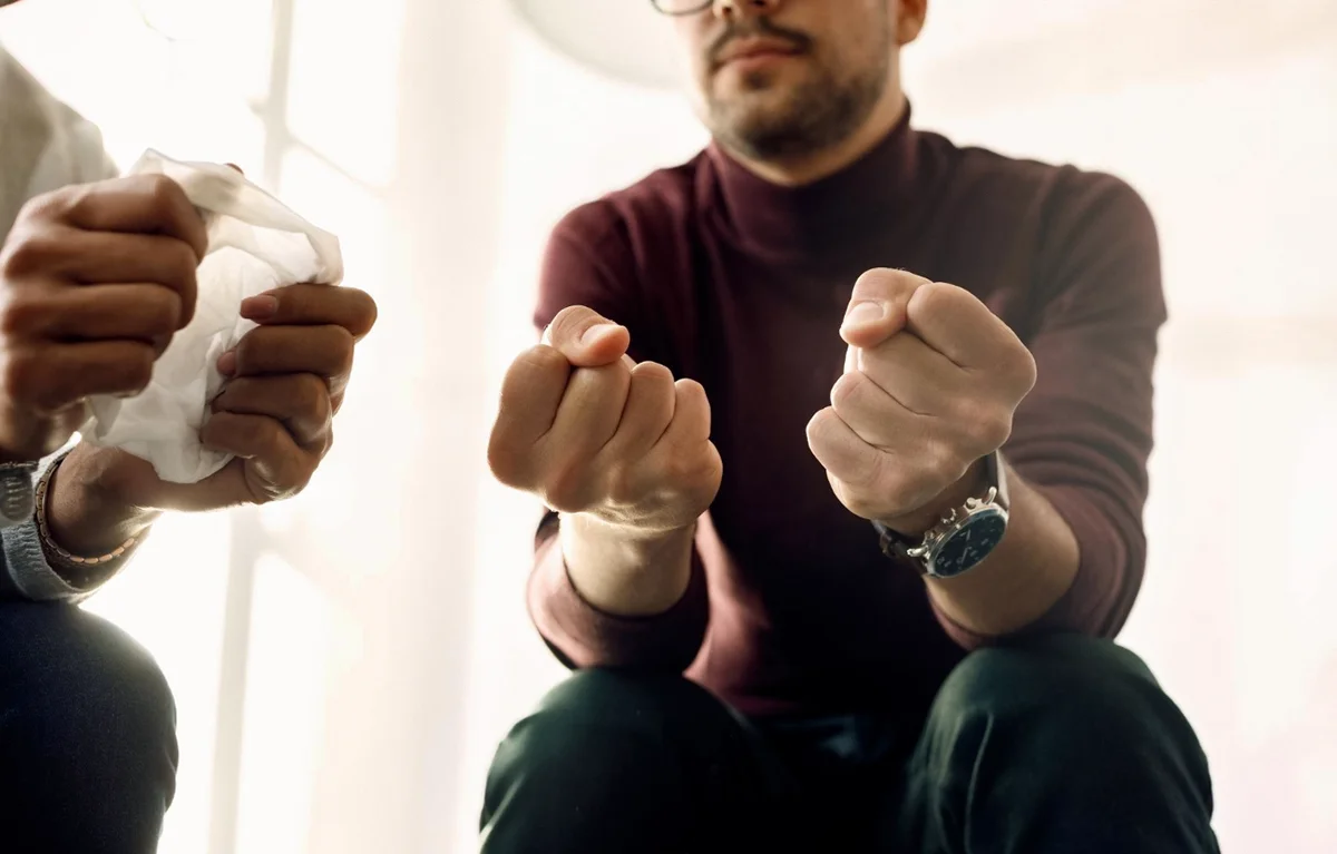 Grupa podrške, muškarac sjedi stisnutih šaka prikazanih u prvom planu; koncept ovisnost o kockanju. ovisnost o kockanju