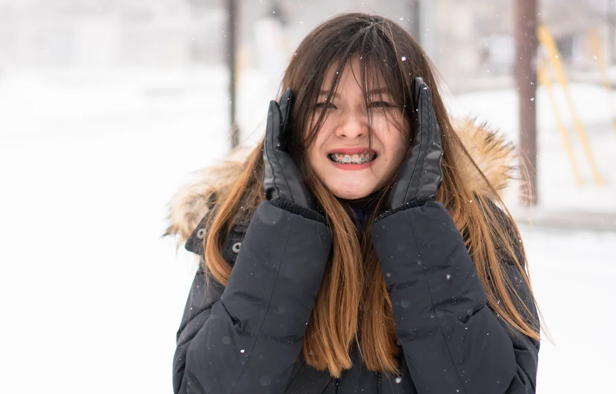 Mlada žena vani na zimskoj hladnoći rukama pokušava ugrijati uši; HZJZ preporuke u hladnoći