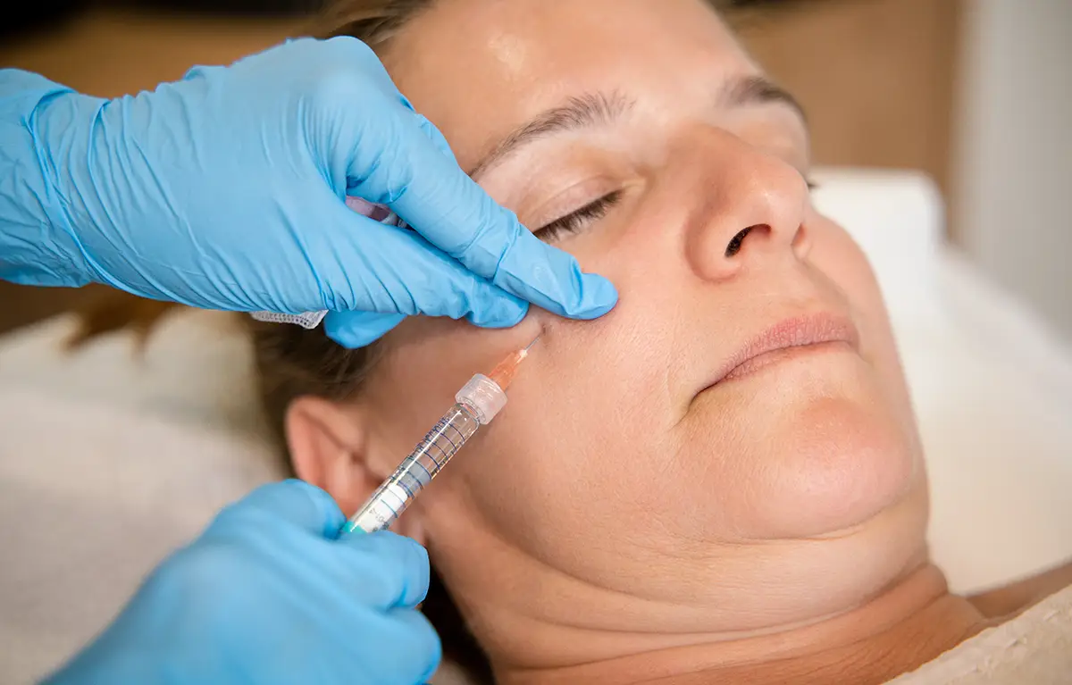 Žena srednje životne dobi žmiri dok prima injekciju botoksa; sigurnost botulin toksina