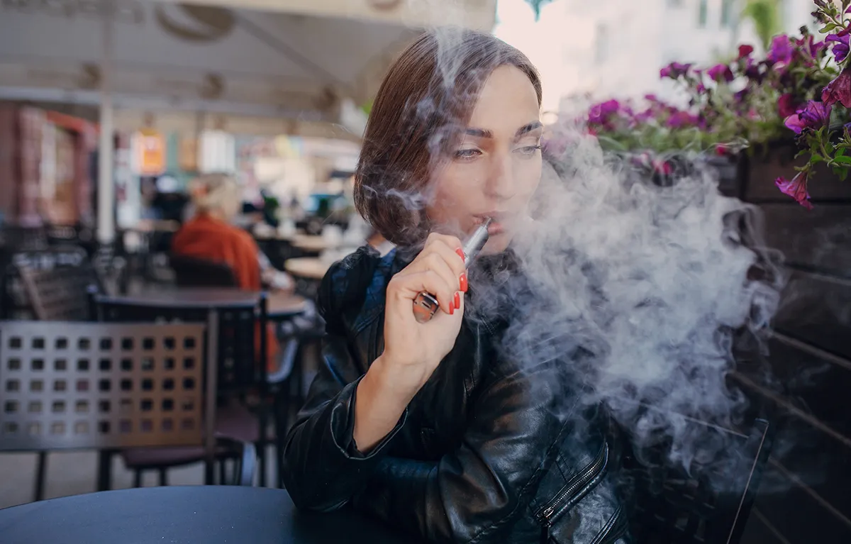 Mlađa žena sjedi u kafiću i puši e-cigaretu