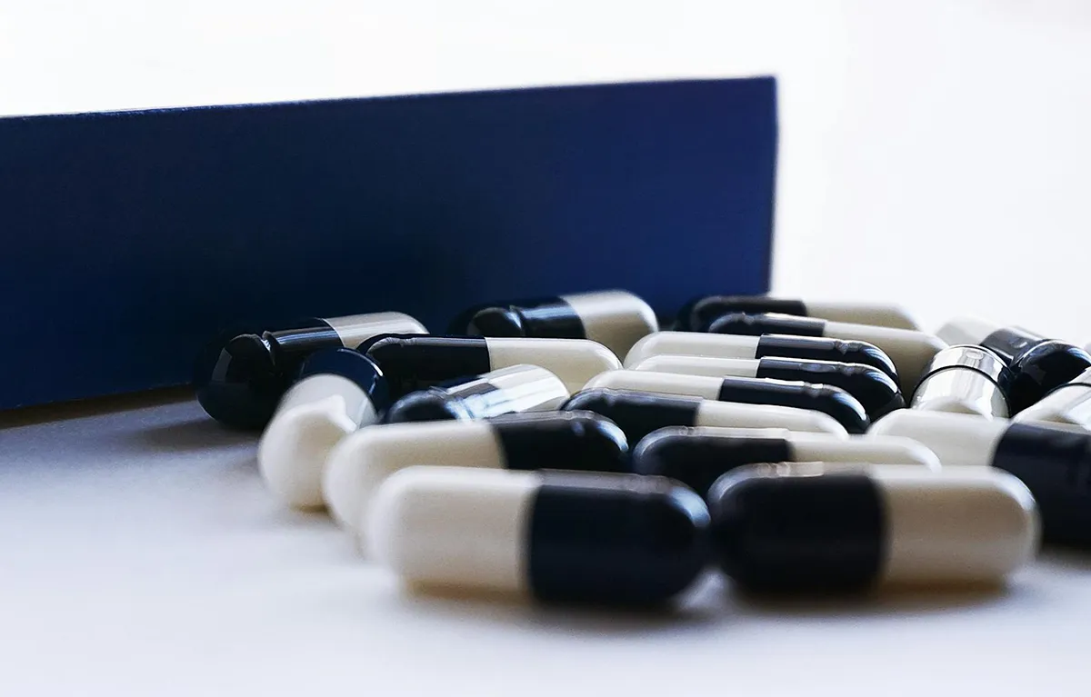 Plavo-bijele kapsule na bijelom stolu uz kutiju tableta