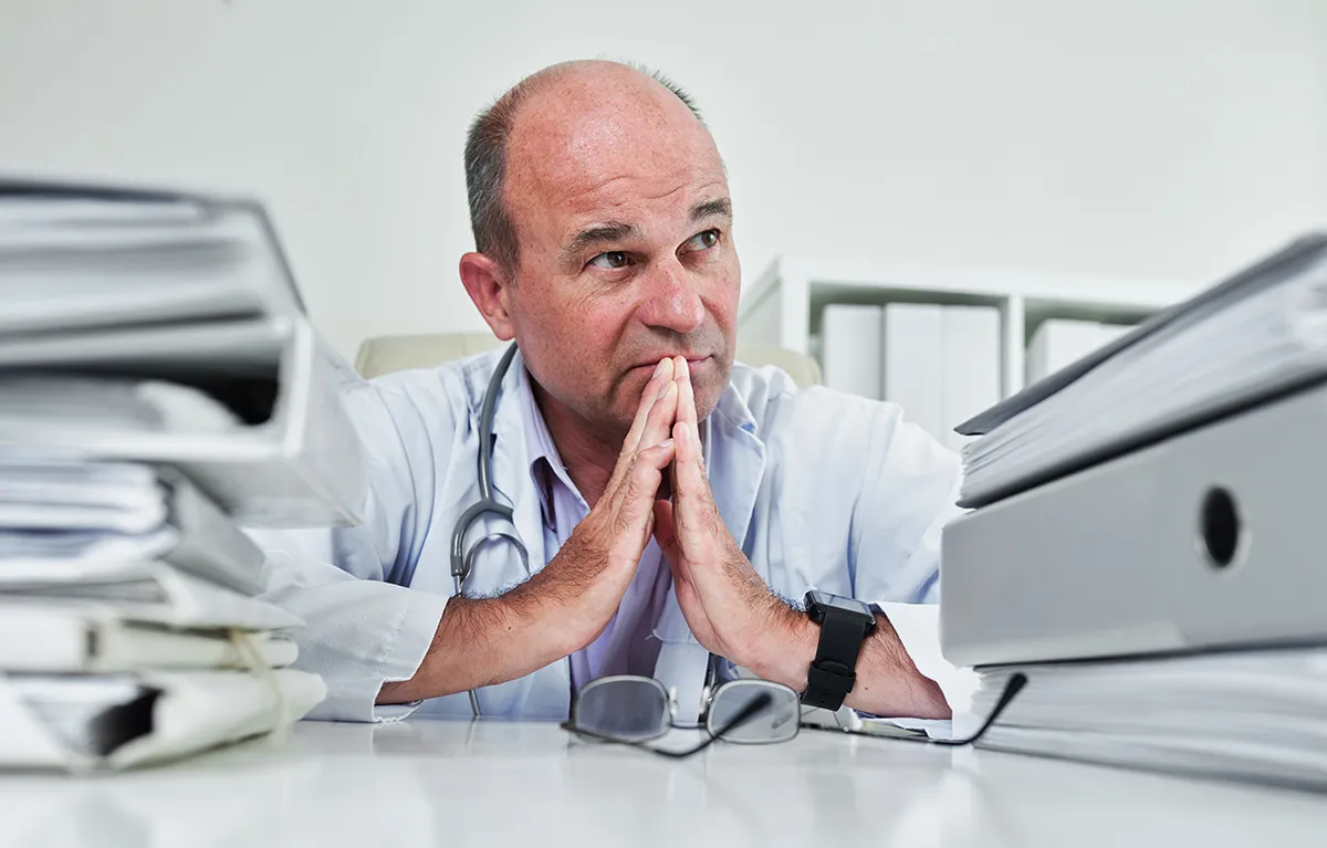 Zabrinut liječnik između gomile papirologije i registratora