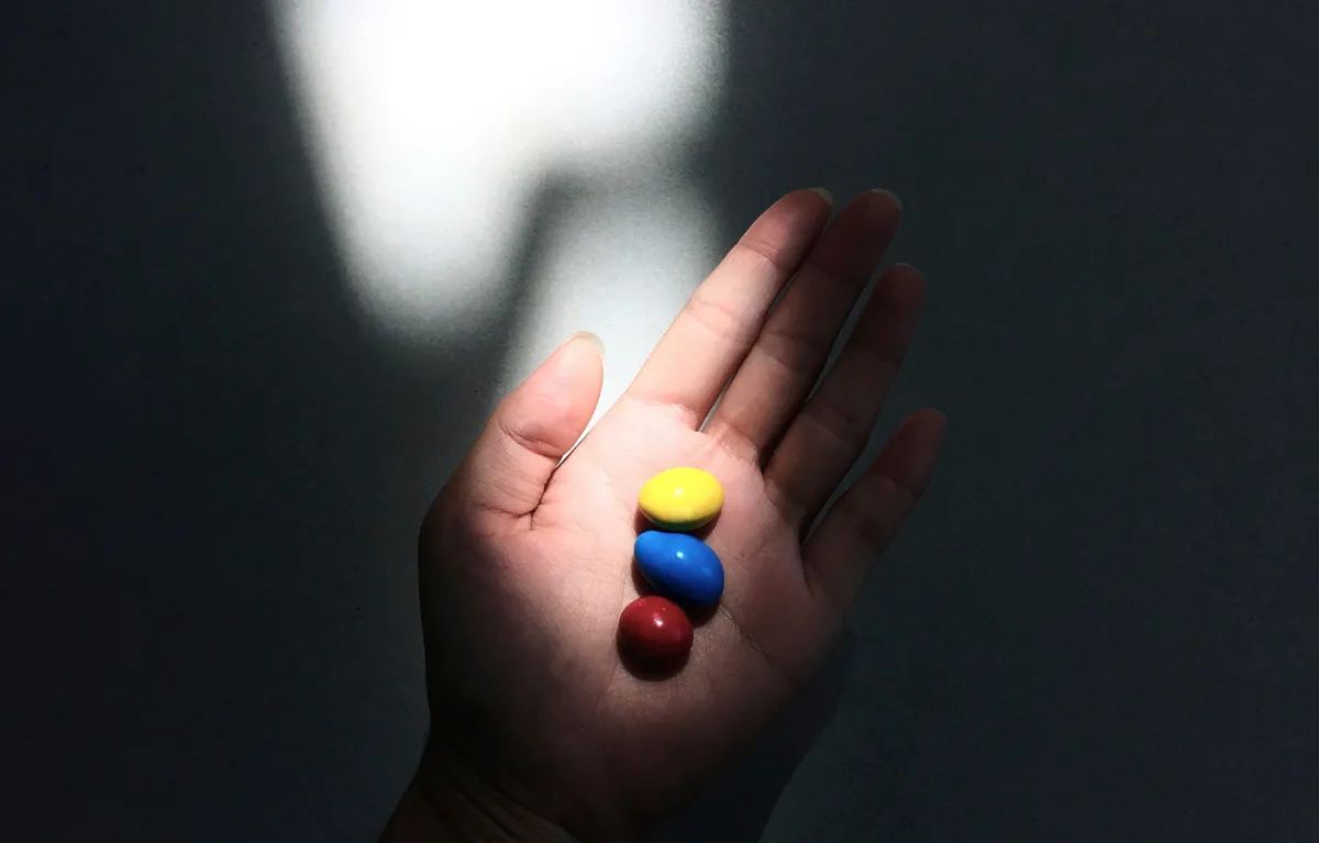 rijetke-bolesti-ruka-lijekovi Na dlanu ruke žuta, plava i crvena tableta, u okruženju dramatičnog svjetla. Koncept rijetke bolesti u Hrvatskoj i broj oboljelih.