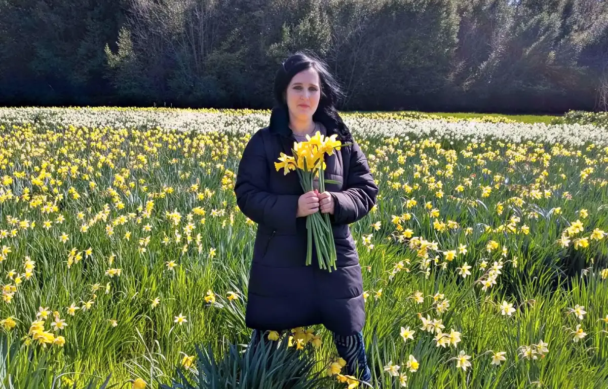 Danijla-Cuk-polje-narcisi Danijela Ćuk stoji u polju narcisa i drži buket cvijeća; napisala je pjesmu za riječku udrugu Nada