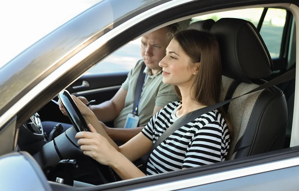 Mlada žena sjedi za volanom auta i uči voziti automobil uz instruktora vožnje; koncept autoškola za osobe s invaliditetom i subvencija koju daje Šibensko-kninska županija